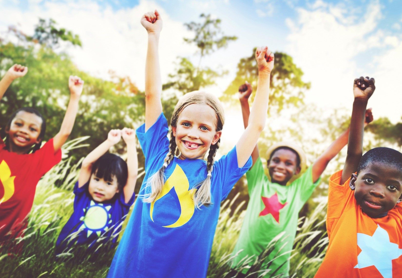 A group of smiling children at summer camp standing outside with their arms up while playing a game. 