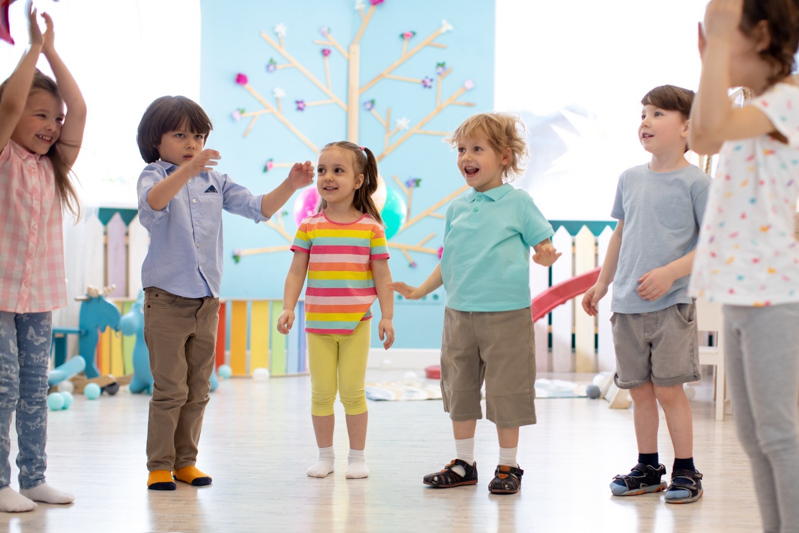 Six children standing in a row in a child care environment playing together. 