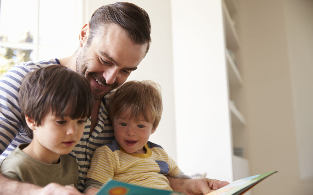 Close Up Of Father And Sons Reading Story At Home Together