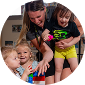 A child care worker laughs with three preschoolers as they play together. 